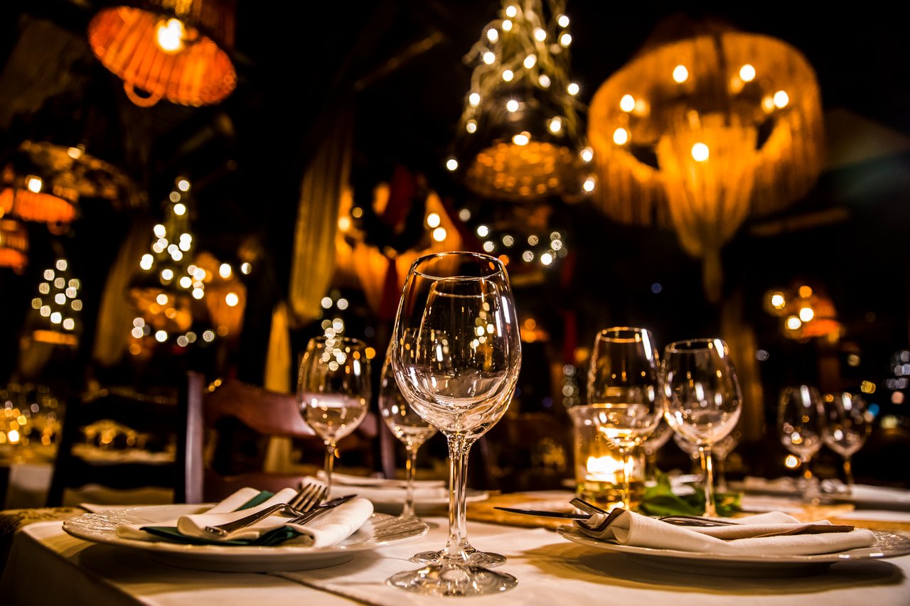 Candlelit fine dining table set with wine glasses and linen napkins beneath warm woven pendant lights in a restaurant dining room