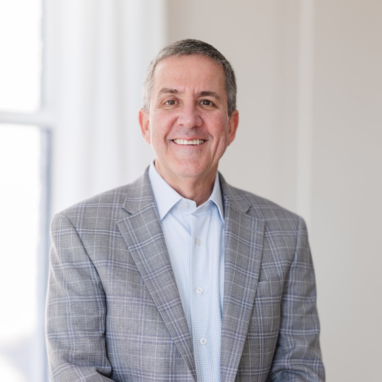 John Pruitt smiling in a gray plaid blazer and light blue shirt.