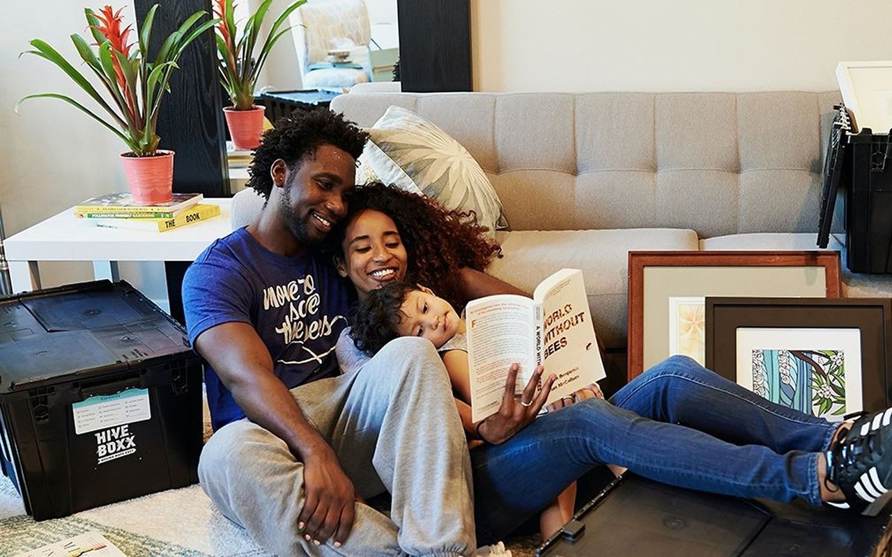 A family reads together beside moving boxes in a furnished living room.