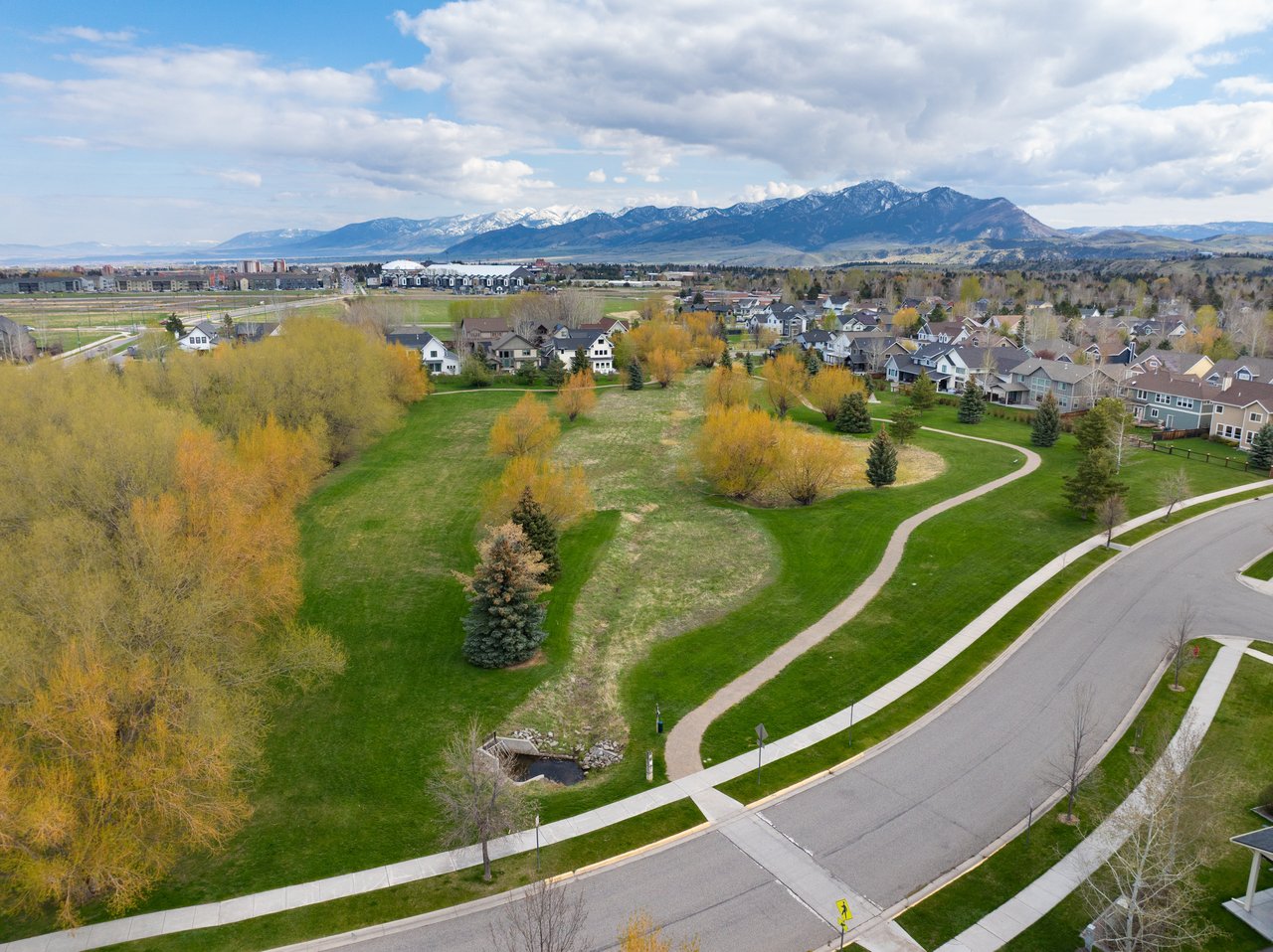 A Bozeman neighborhood and park with a winding path, backed by the snow-dusted Bridger Mountains.
