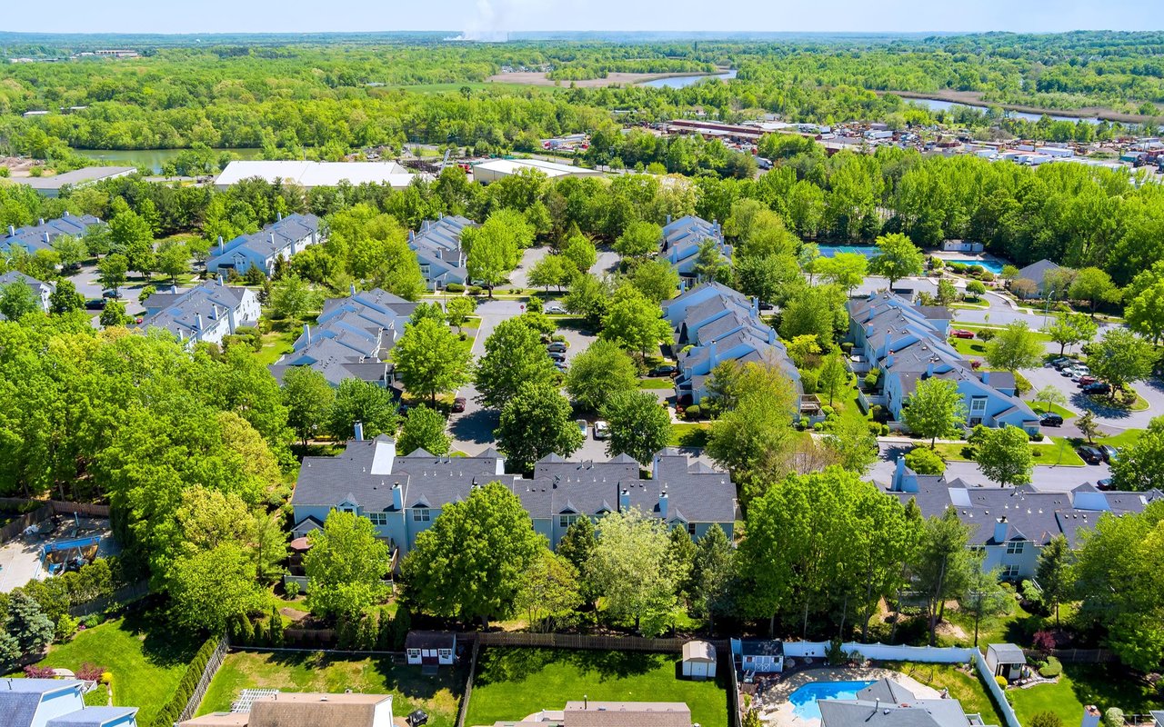 Aerial view of tree-lined townhomes with swimming pools and water in the distance.
