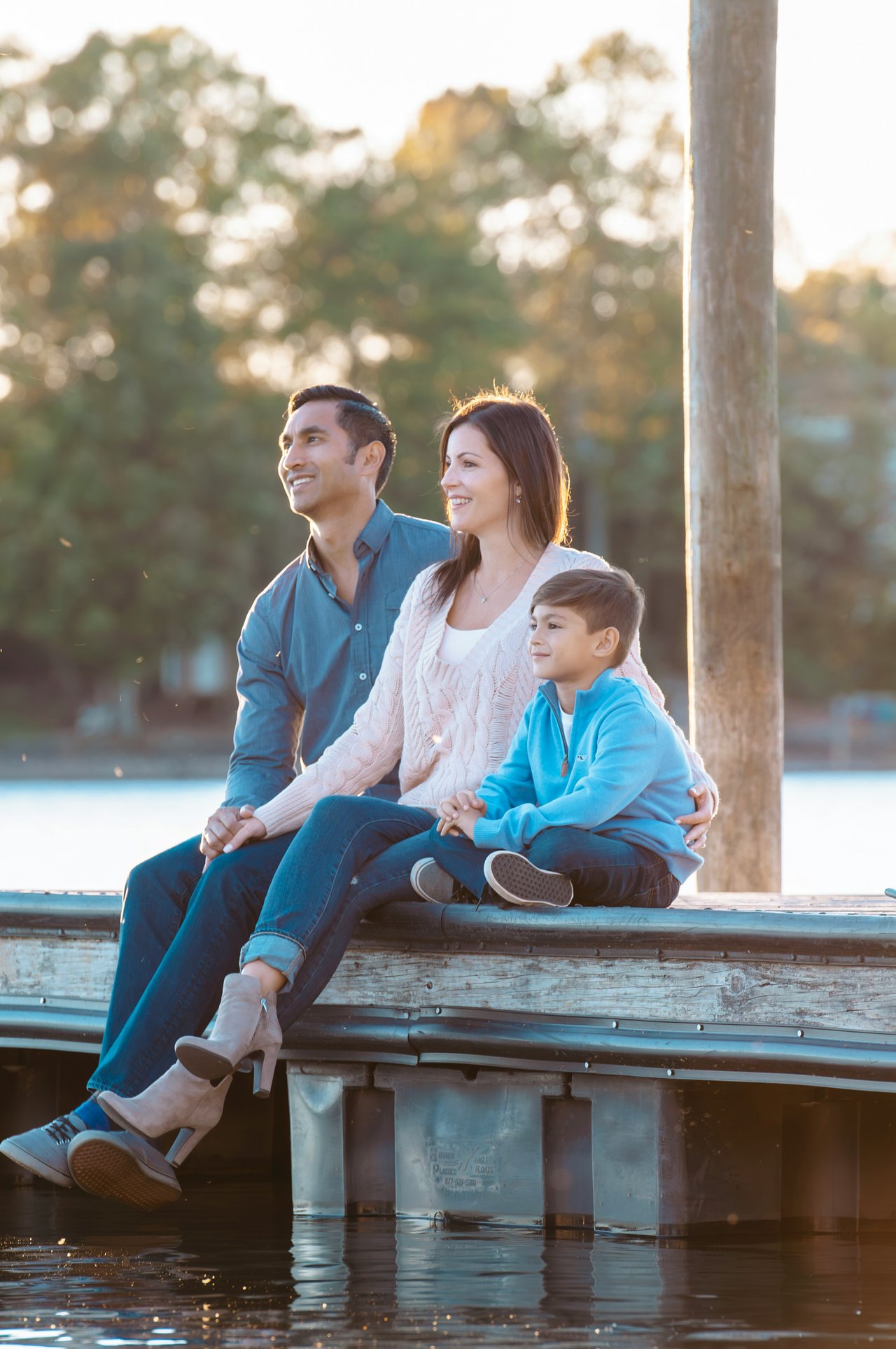 Family sitting together on a lakeside dock in warm evening light.