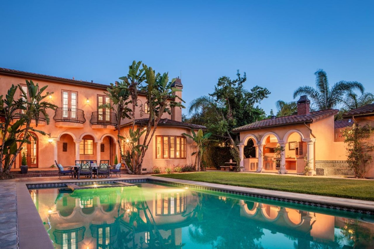 Mediterranean-style stucco home with a pool and illuminated outdoor kitchen at dusk.