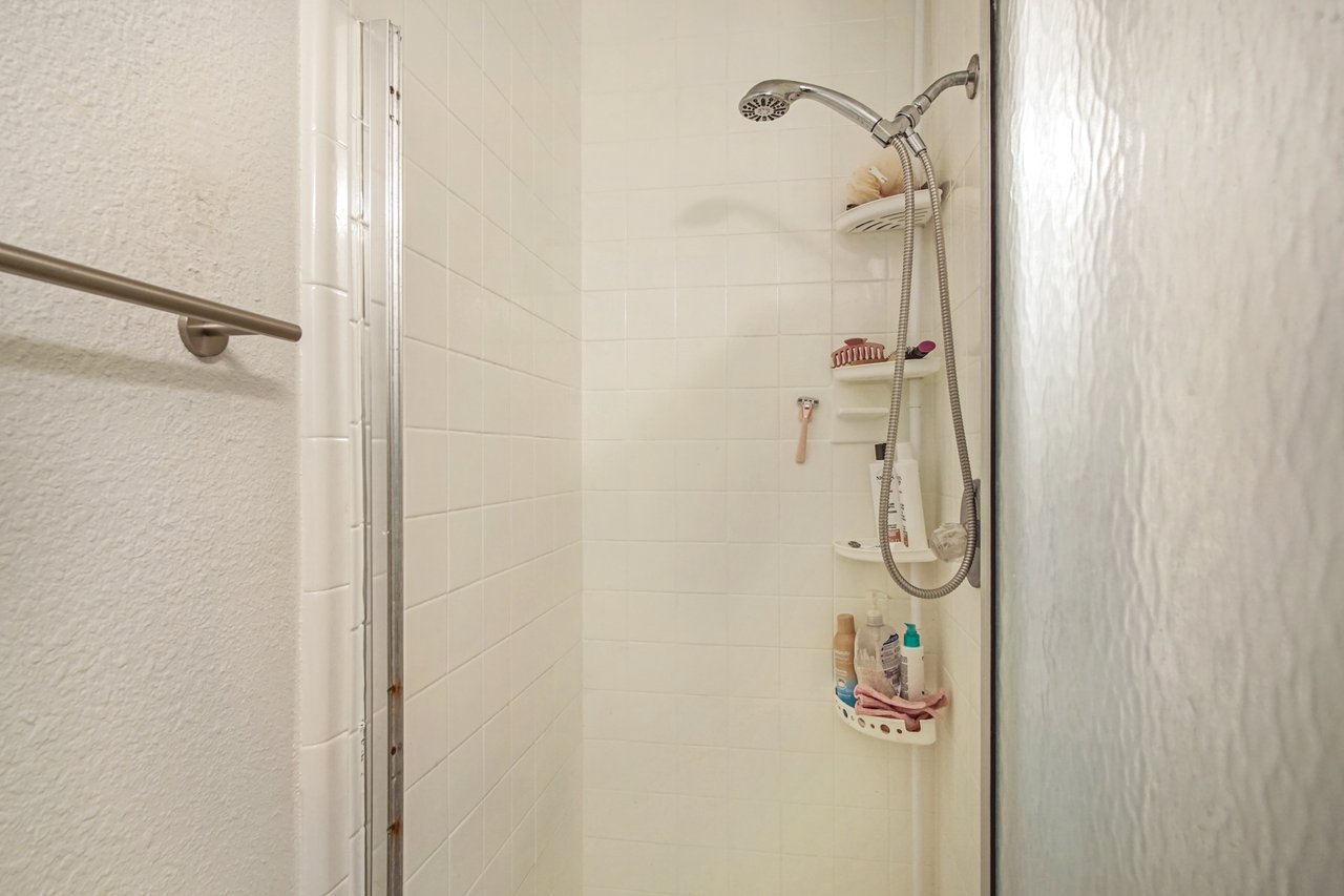 Shower interior with white tiles and a silver showerhead. Shelves hold toiletries and a pink razor. A towel bar is mounted on the left wall. Minimalist and clean.Shower interior with white tiles and a silver showerhead. Shelves hold toiletries and a pink razor. A towel bar is mounted on the left wall. Minimalist and clean.