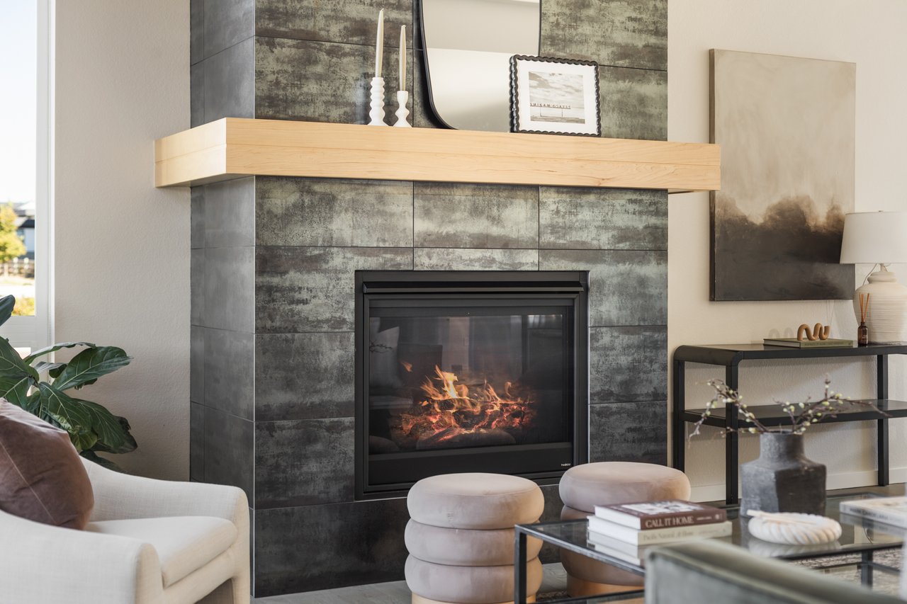 Fireplace with a dark tile surround and floating wood mantel beside a cream accent chair