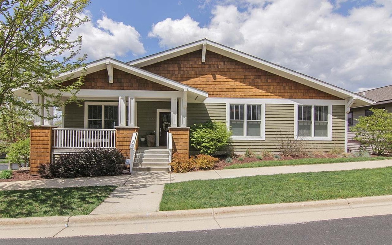 Single-story olive-green home with brown shingle gables and a covered front porch.