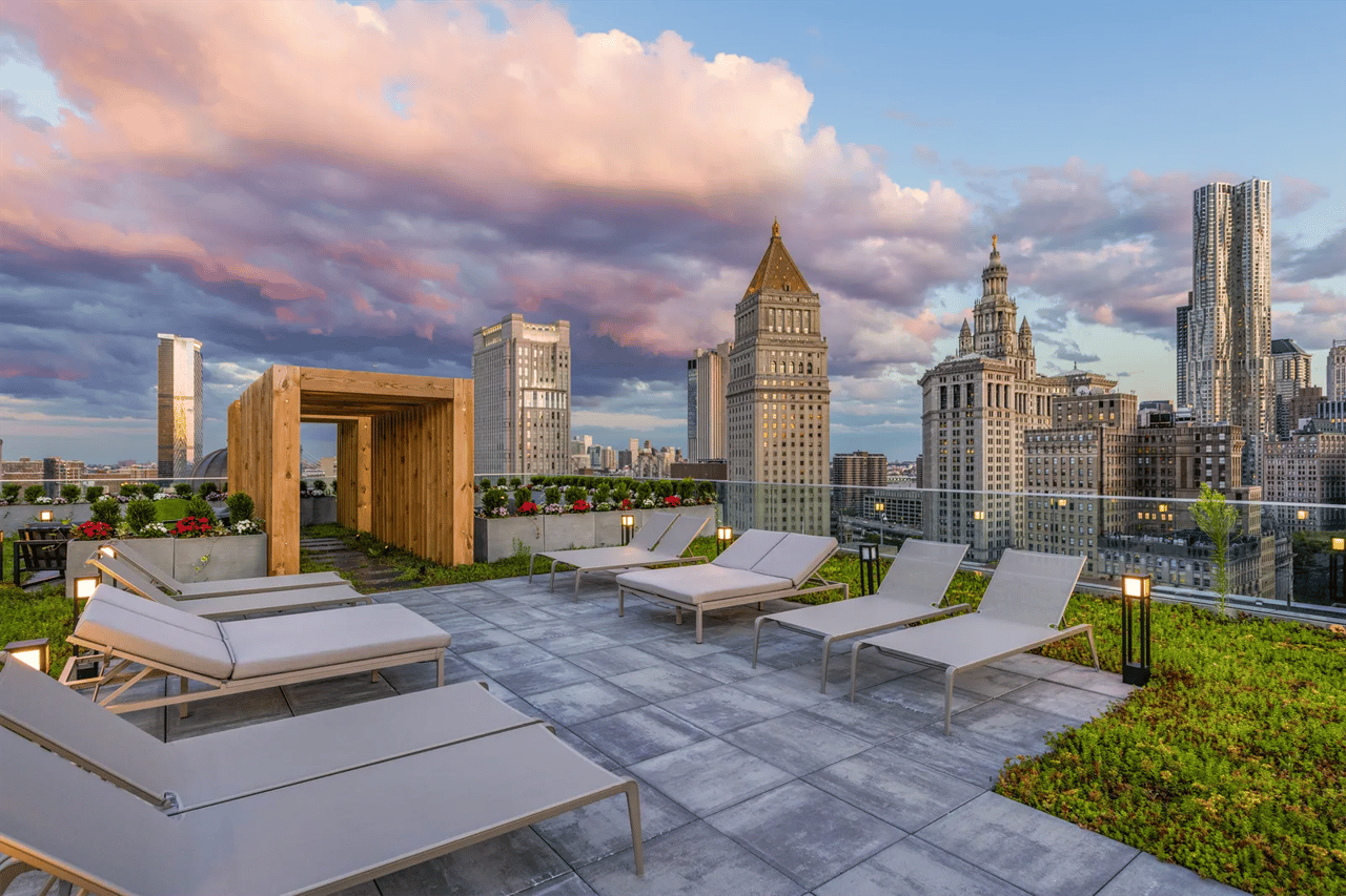Rooftop terrace with lounge chairs and landscaped planters overlooking the Manhattan skyline.