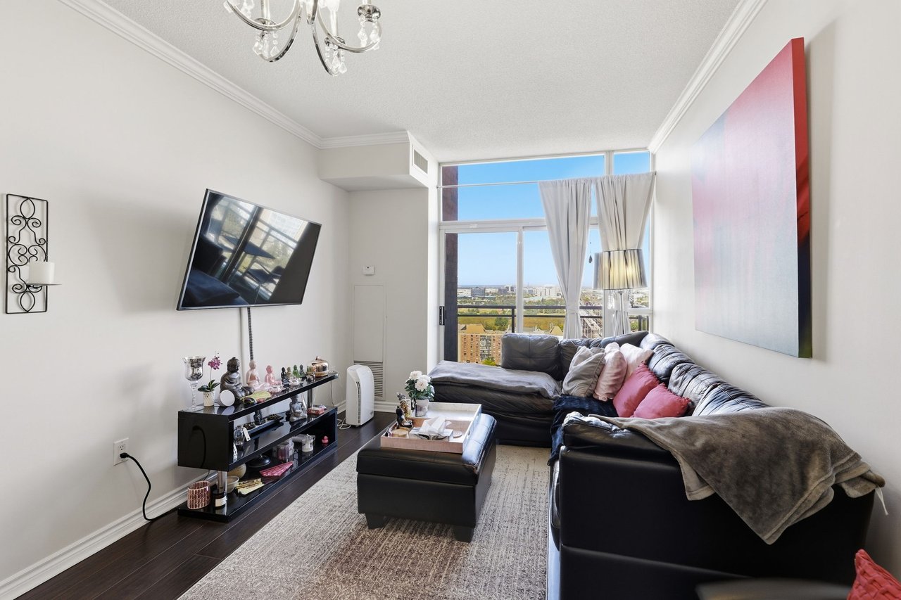 Living room with a black leather sectional, wall-mounted TV, and large windows overlooking the city.