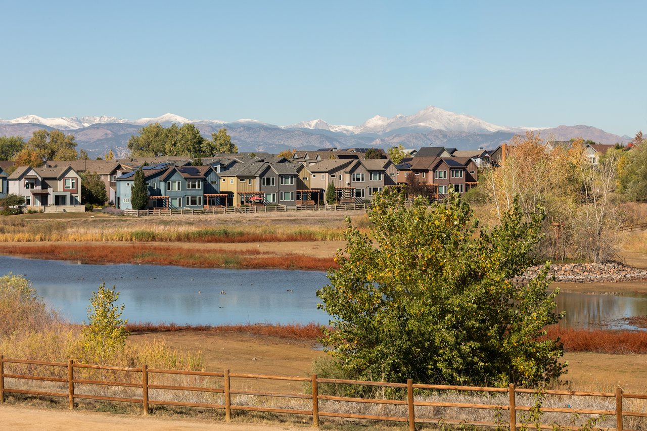Lake view with snow-capped mountains behind neighborhood homes and a wood rail fence