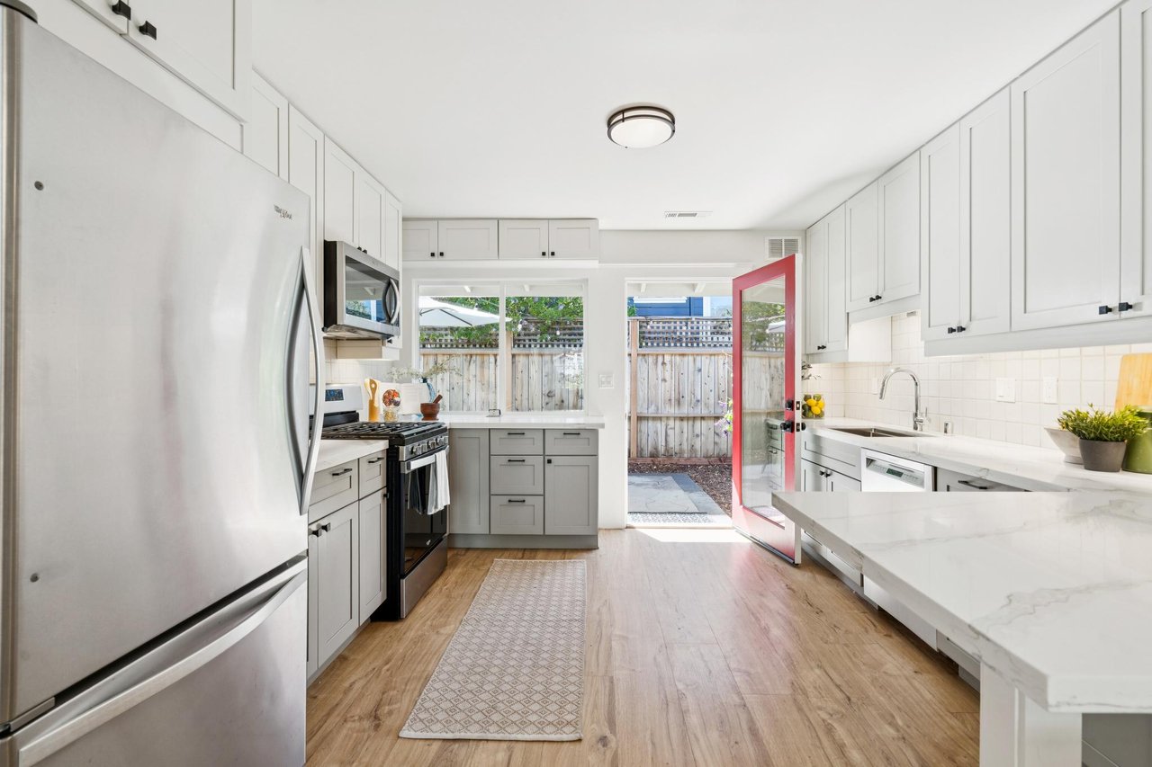 Bright white kitchen with stainless steel appliances and a red door opening to a fenced patio.