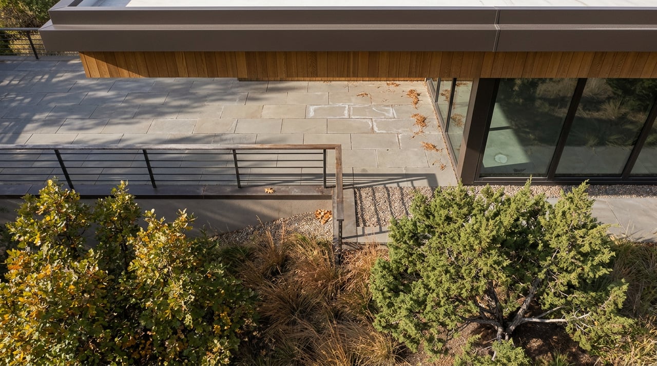 Stone terrace beneath a cedar roof overhang overlooks a slope with juniper, bronze grasses, and autumn oaks.