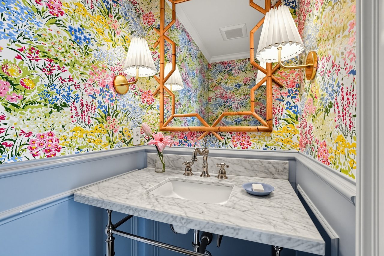 Powder room with a marble vanity, floral wallpaper, and a geometric wood-framed mirror.