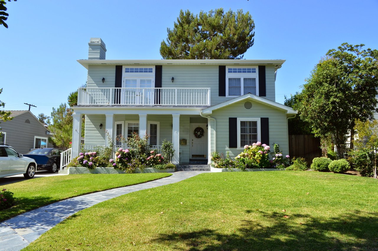 Mesa Verde two-story home with a white balcony, flowering shrubs, and a stone walkway.