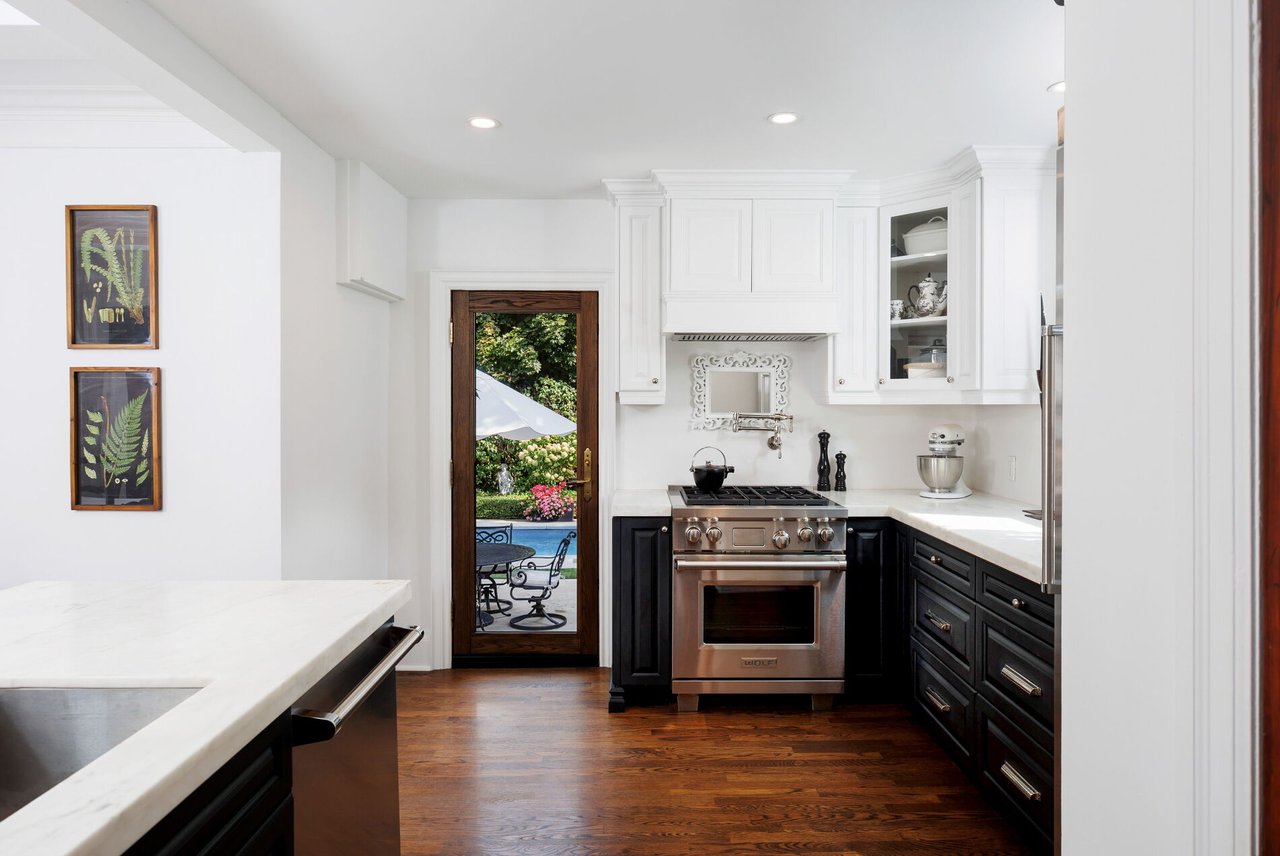 Kitchen with white cabinetry, dark lower cabinets, marble counters, and a glass door overlooking a garden pool.