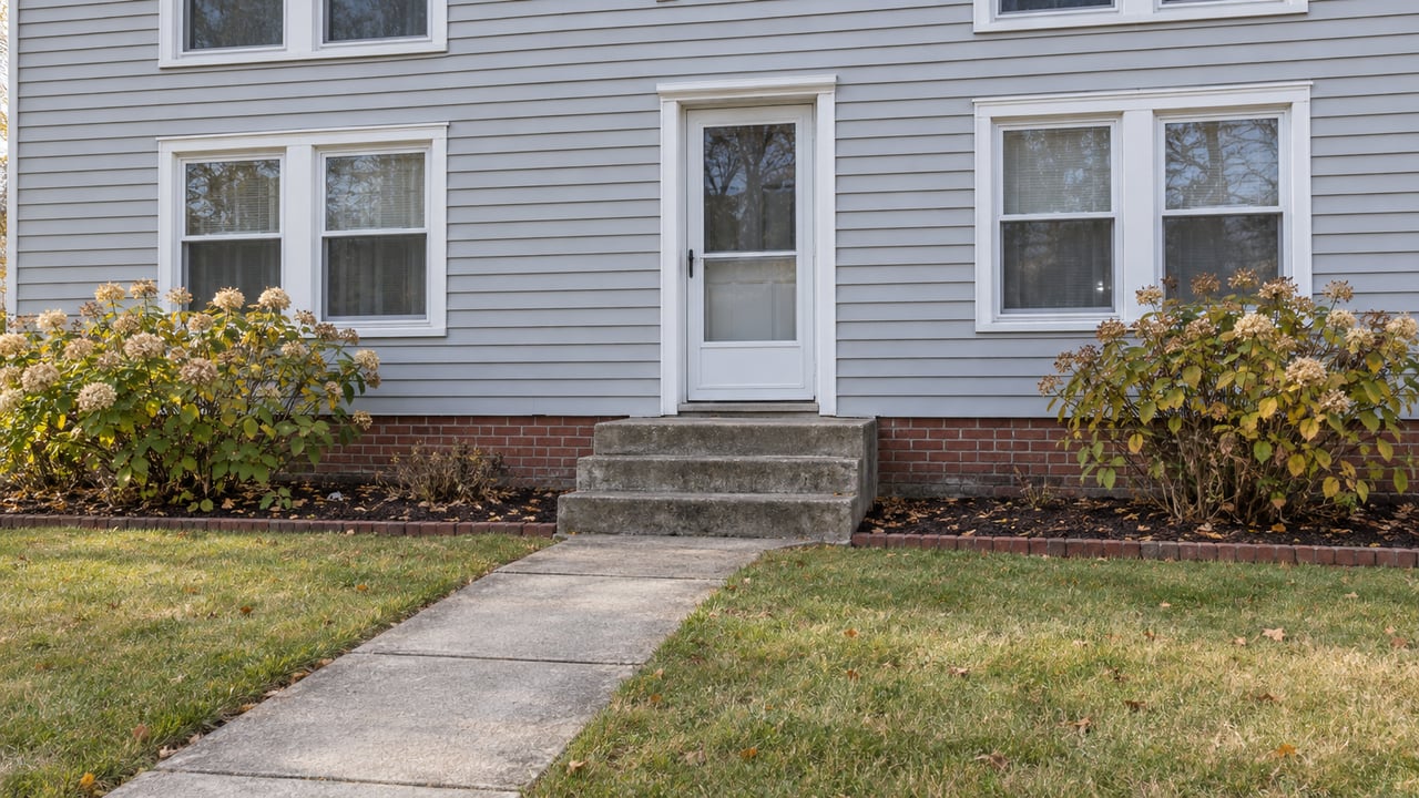 Light gray two-story house with white-trimmed windows, brick foundation, concrete front walk and two autumn hydrangeas.