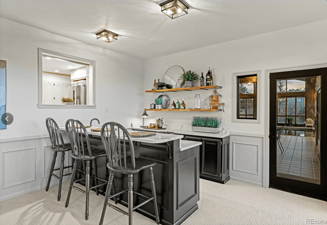 Kitchen with a dark island, three bar stools, open shelves, and a glass door to a sunroom.