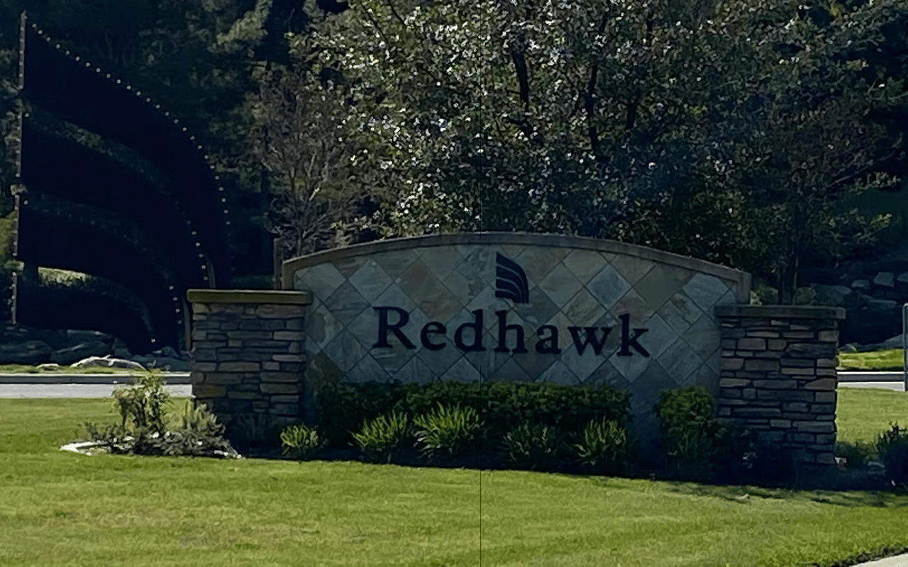 Redhawk community entrance sign set on a landscaped lawn beneath mature trees.