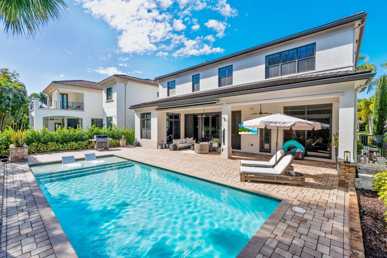 Two-story white home with a covered patio behind a swimming pool and paved deck.