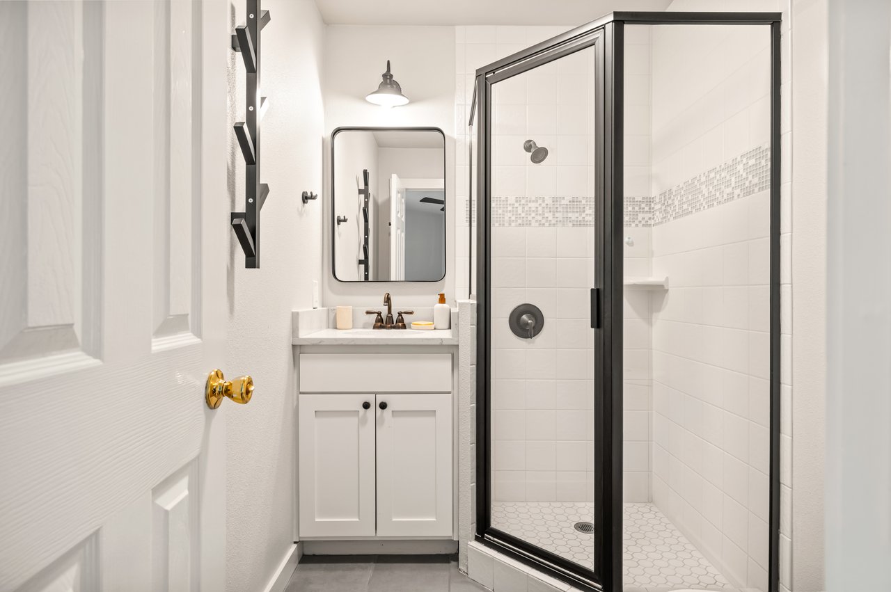 Bathroom with a black-framed glass shower, mosaic accent tile, and white vanity.