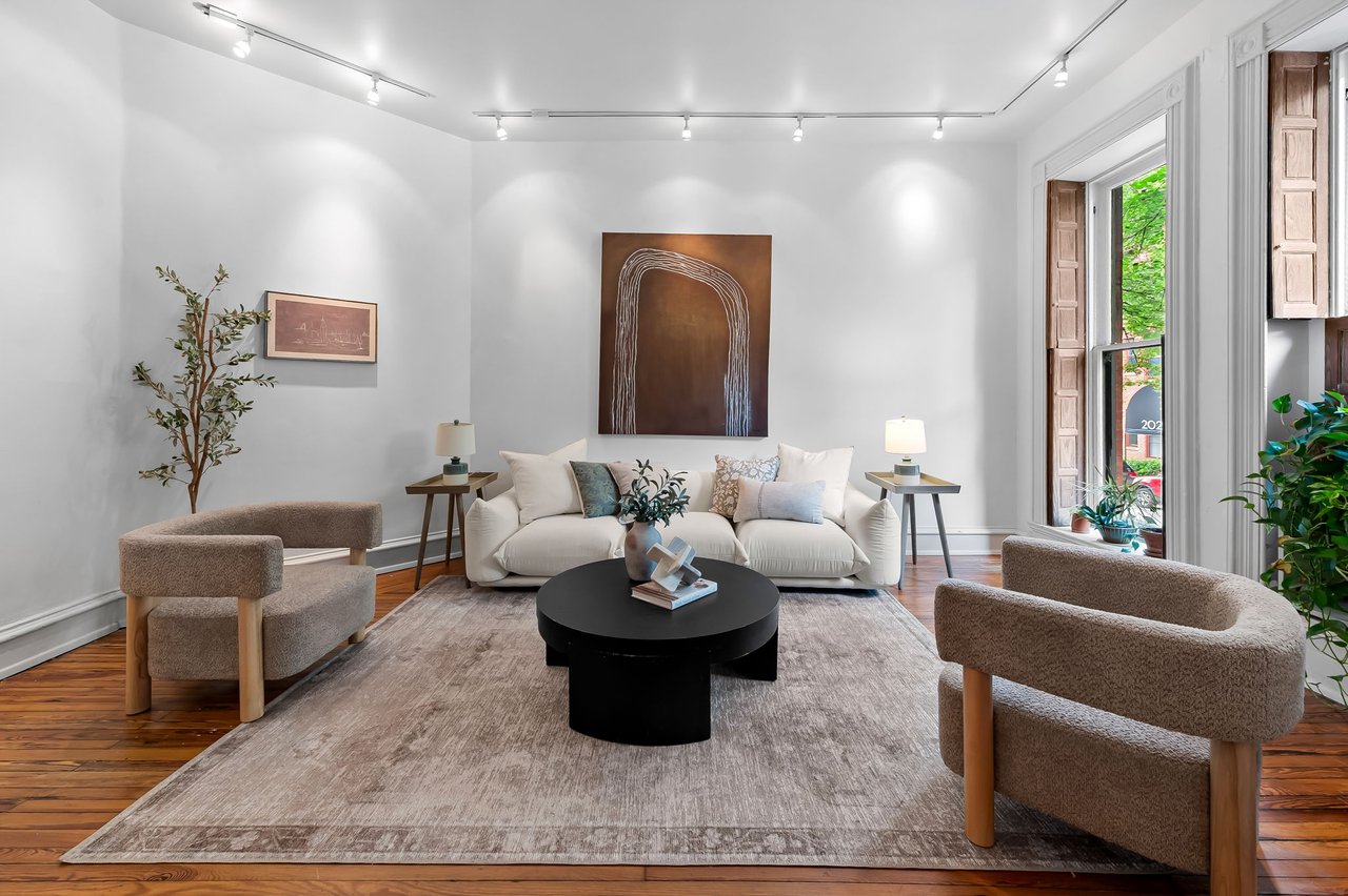 Staged living room with a white sofa, sculptural black coffee table, and tall shuttered windows.