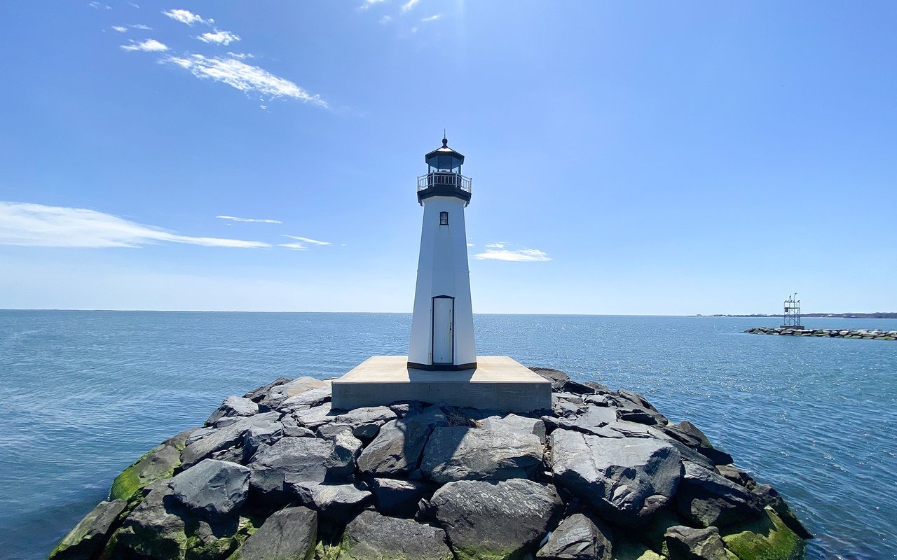 White lighthouse at the end of a rocky breakwater over blue water