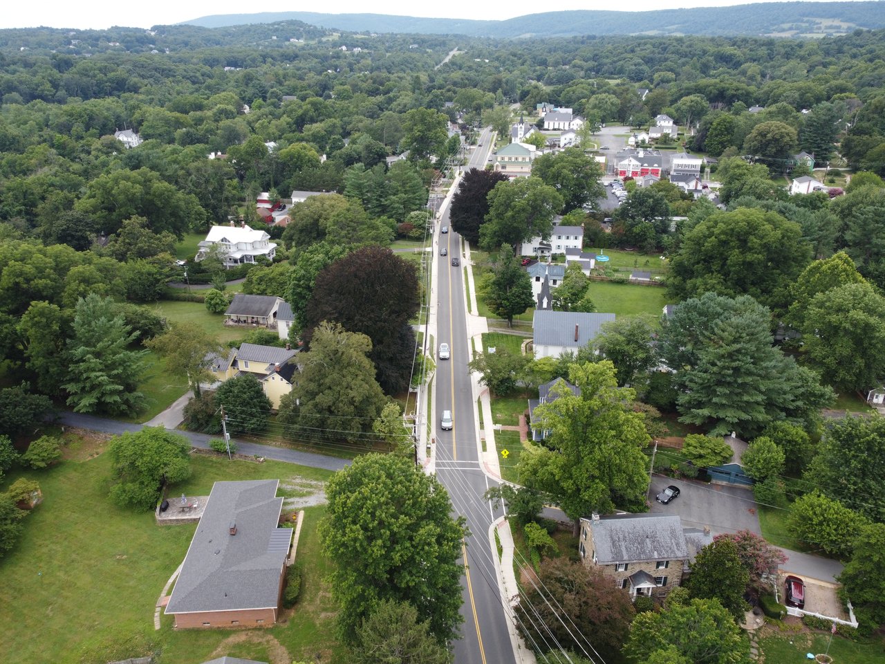 An elevated aerial drone shot capturing the historic residential streets, mature tree canopy, and scenic countryside of Round Hill, VA in Western Loudoun County, photographed by local real estate expert Diana Geremia.