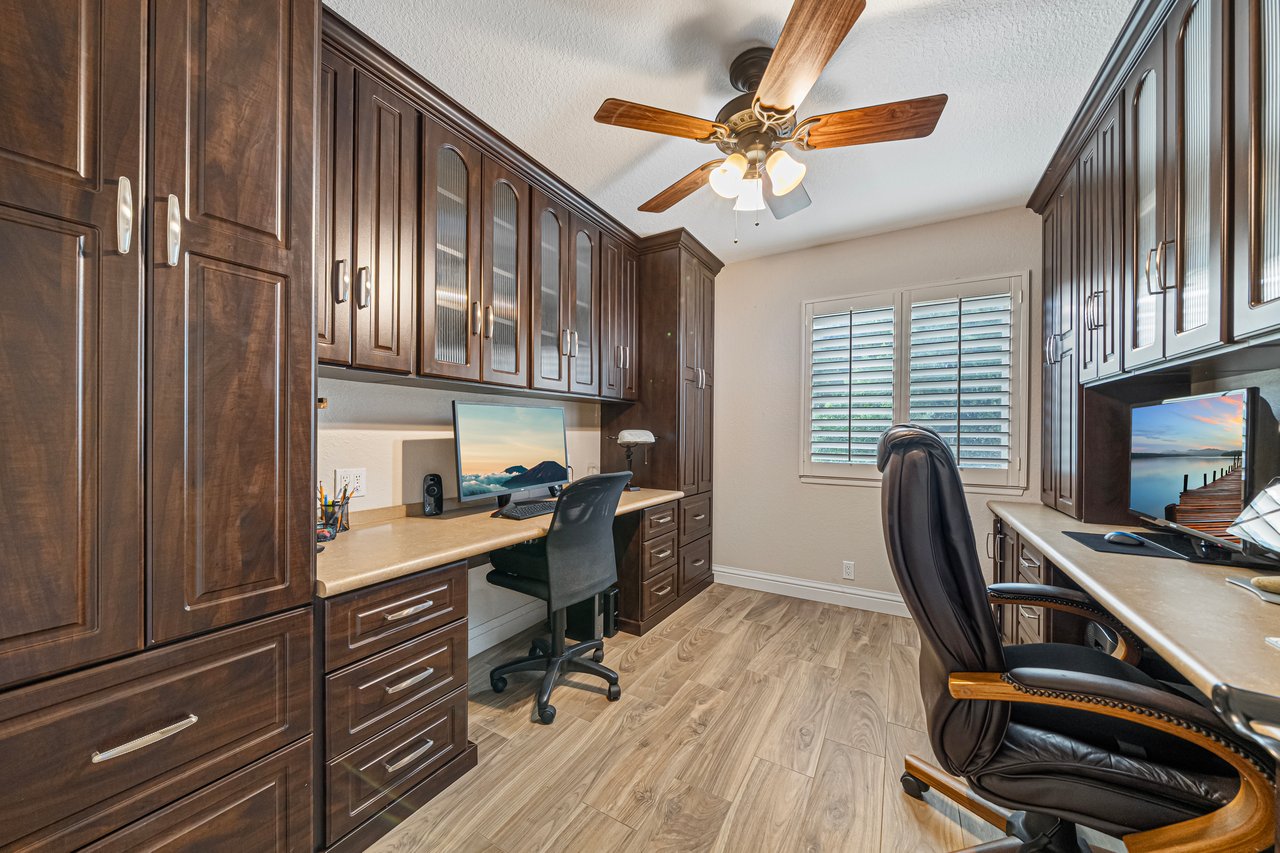 Home office with dark wood built-in cabinets, desks on both sides, and shuttered windows.