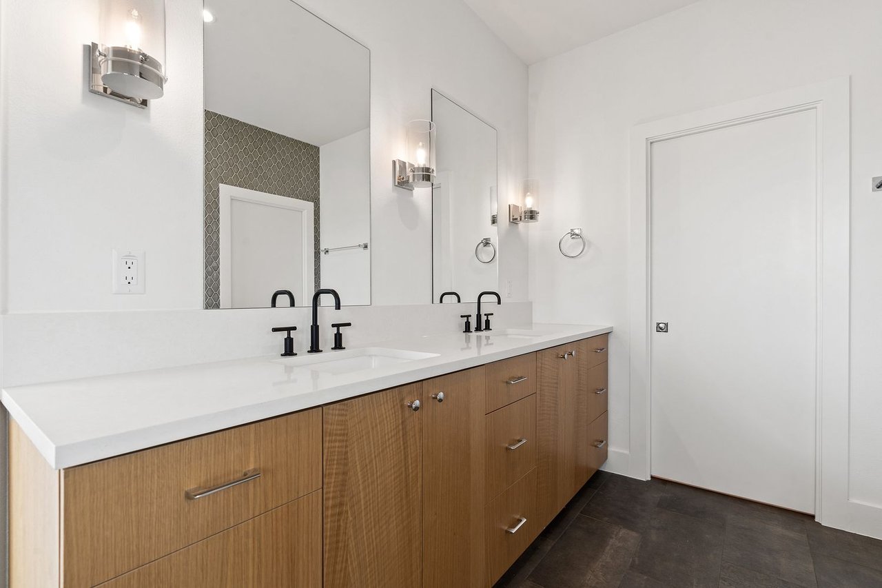 Bathroom with a long double vanity, wood cabinetry, black faucets, and large mirrors.