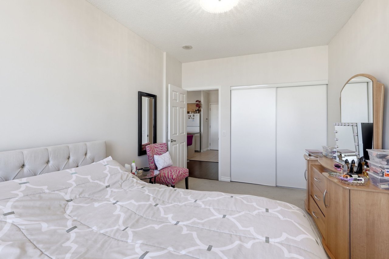 Furnished bedroom with a patterned bed, sliding-door closets, and a dresser with mirrors.