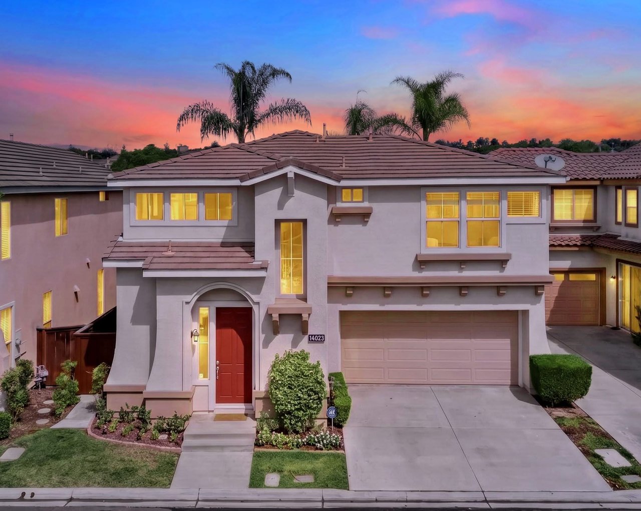 Two-story stucco home with a red front door and lit windows at dusk.