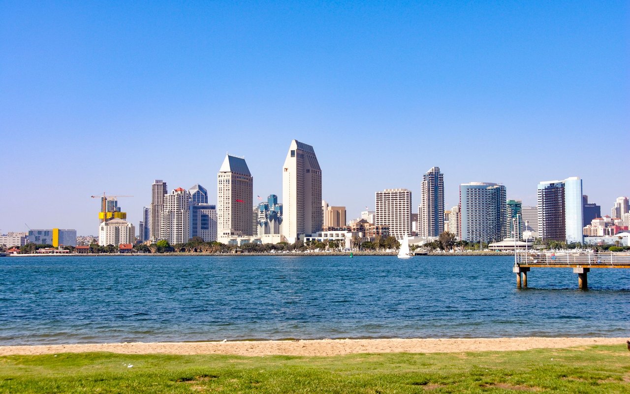 Downtown San Diego skyline across the bay, viewed from a sandy waterfront with a pier.