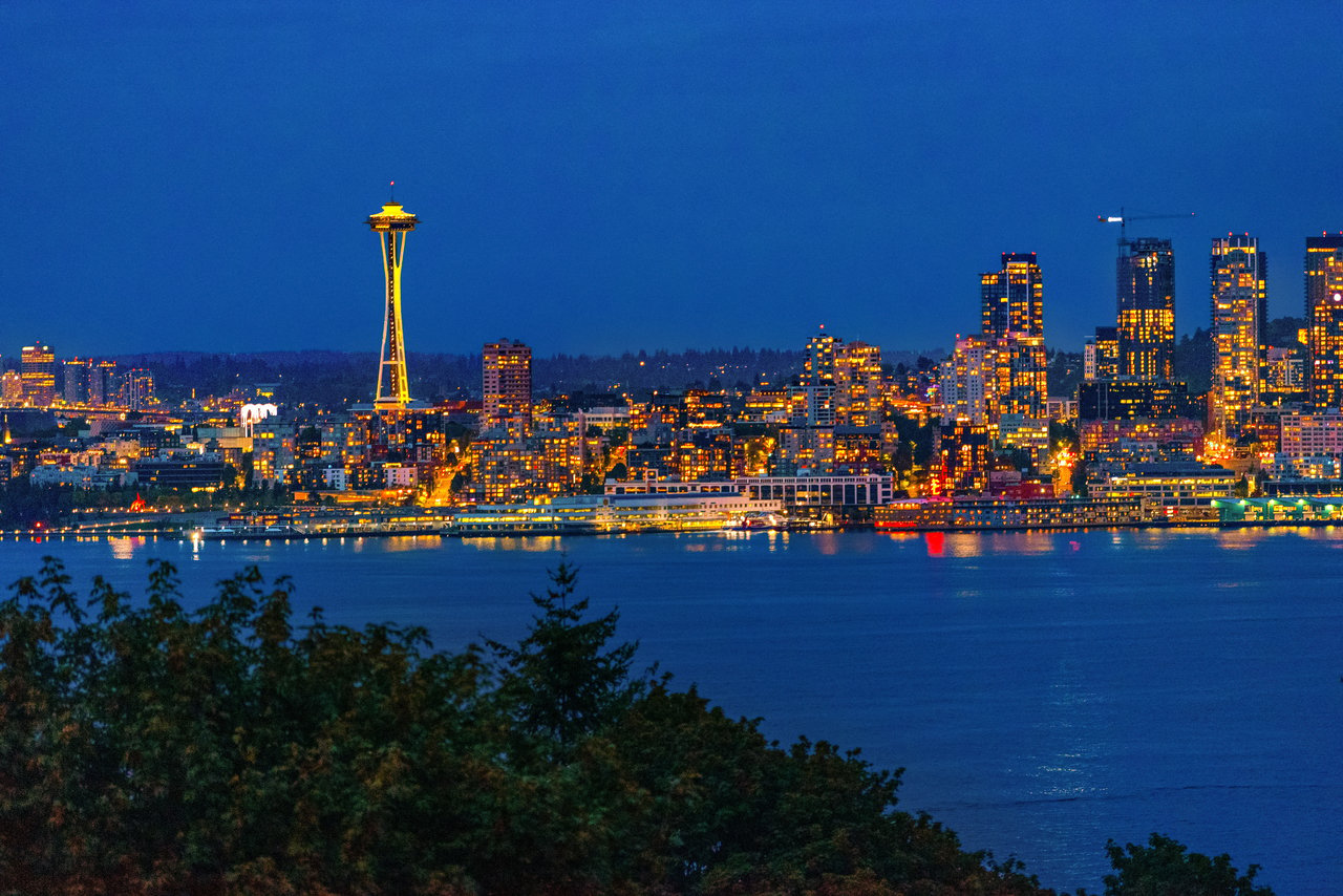Seattle skyline at night across Elliott Bay, with the illuminated Space Needle and downtown towers.