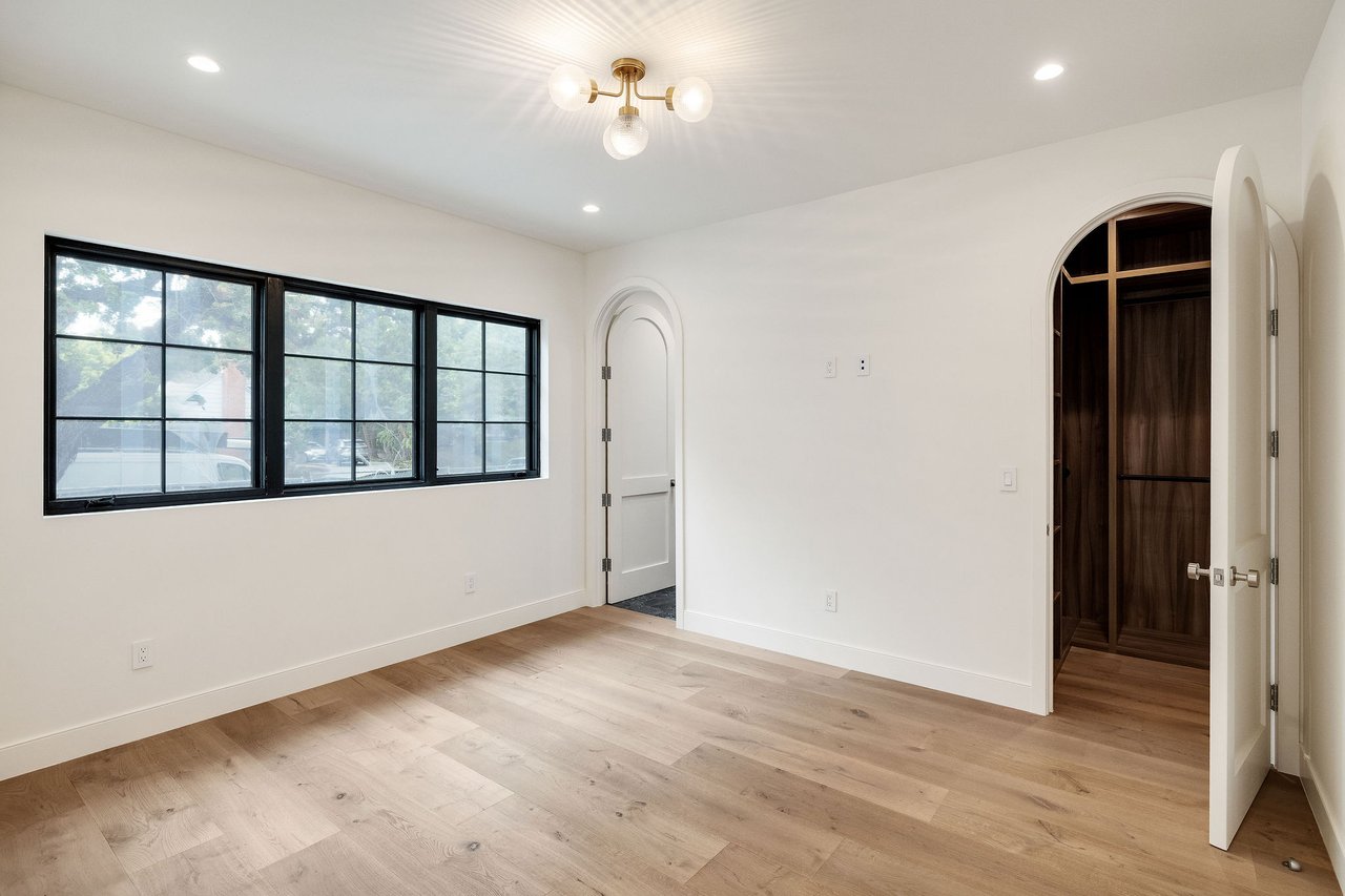 Vacant bedroom with black-framed windows, pale wood floors, and an arched dark-wood closet.