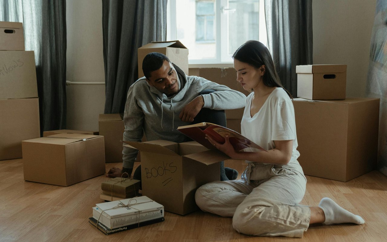Couple packing among moving boxes, pausing to look through a book.