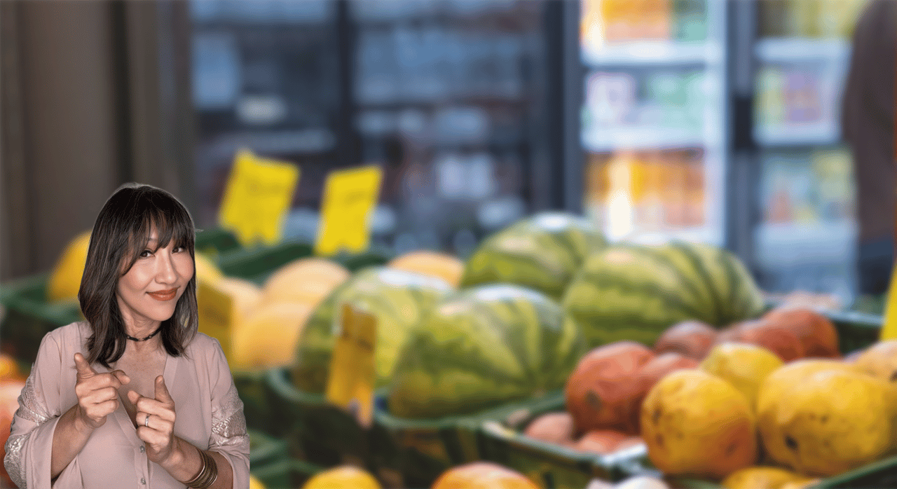 Woman pointing in front of a grocery produce section with watermelons and other fruit.