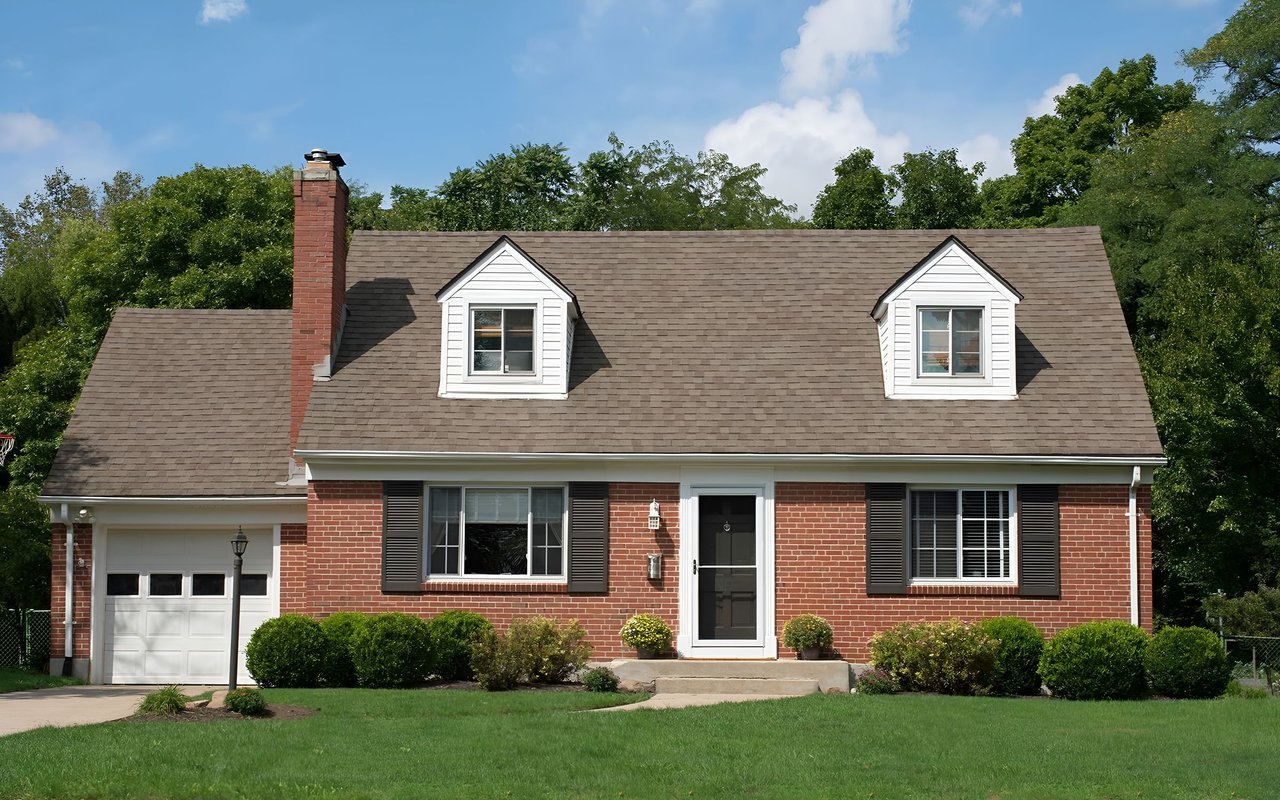 Red brick house with two roof dormers, an attached garage, and a broad green lawn.
