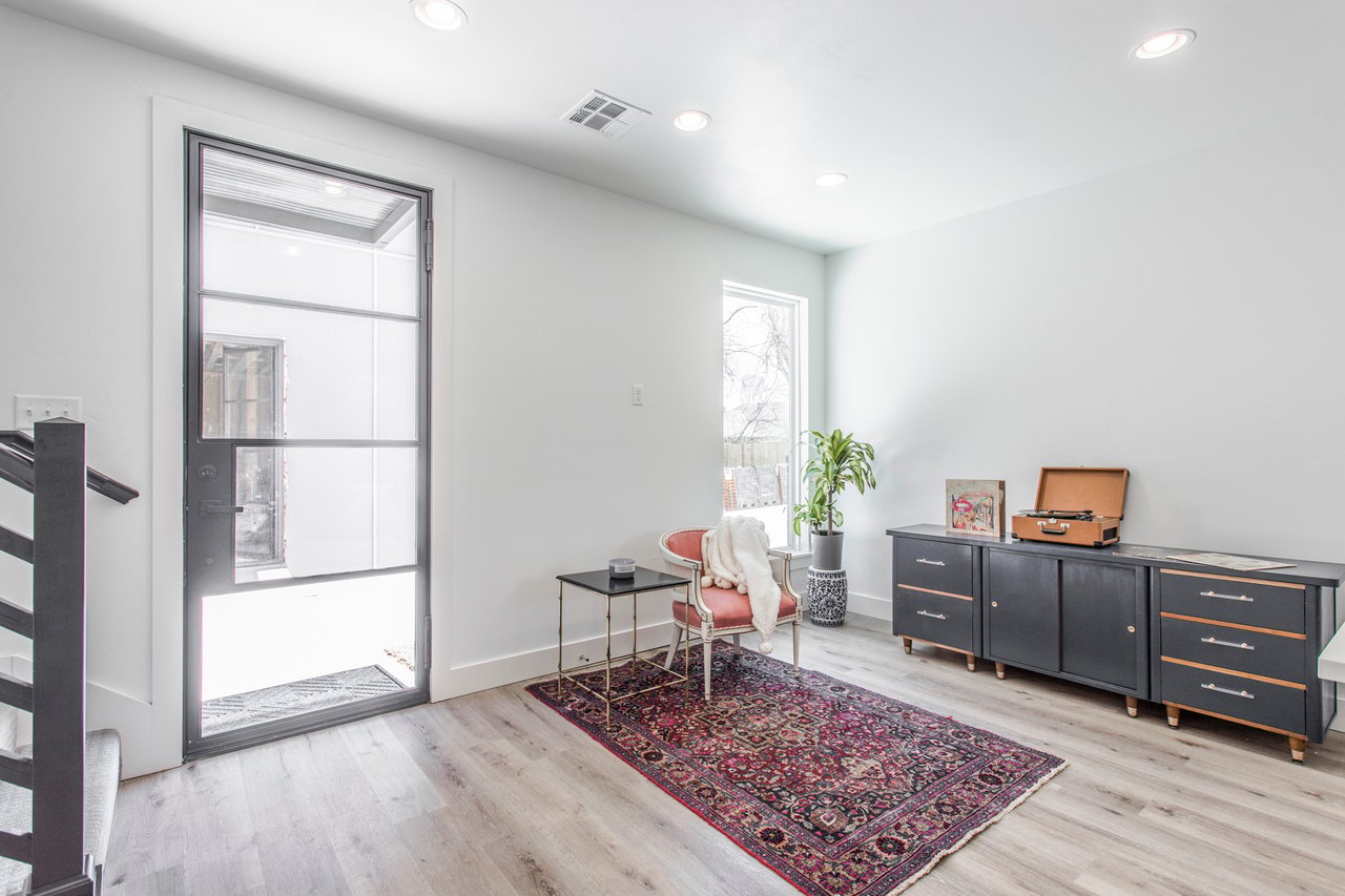 Bright sitting area with a glass-paneled door, red chair, patterned rug, and black sideboard.