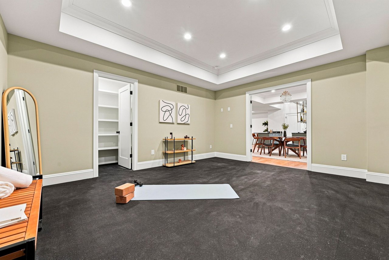 Exercise room with dark carpet, a tray ceiling, and a yoga mat beside an open dining-room doorway.