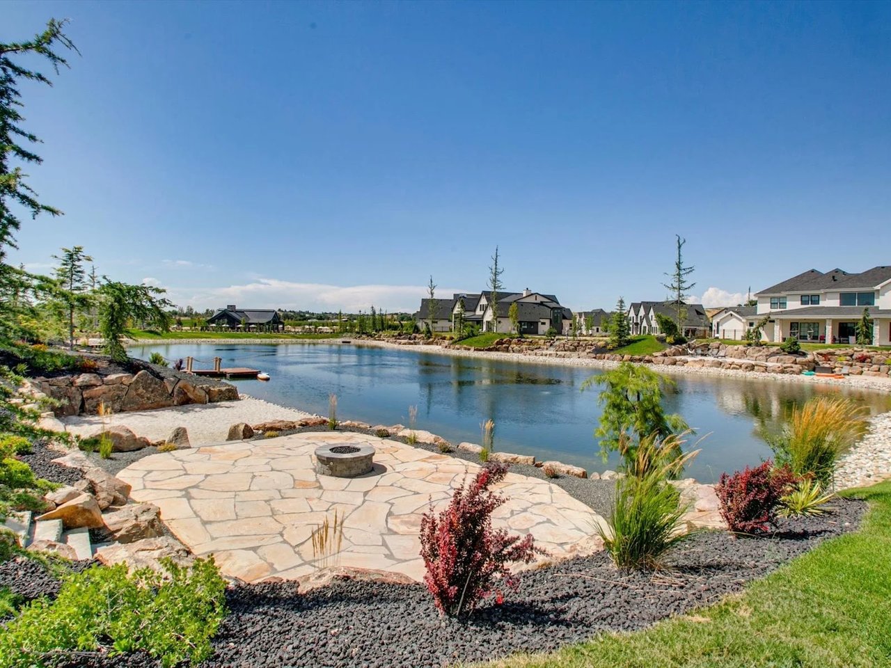 Neighborhood pond bordered by homes, with a stone patio and fire pit in the foreground.