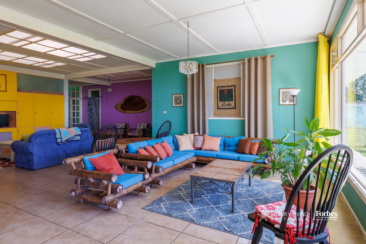 Living room with blue seating, colorful walls, yellow cabinets, and large windows.