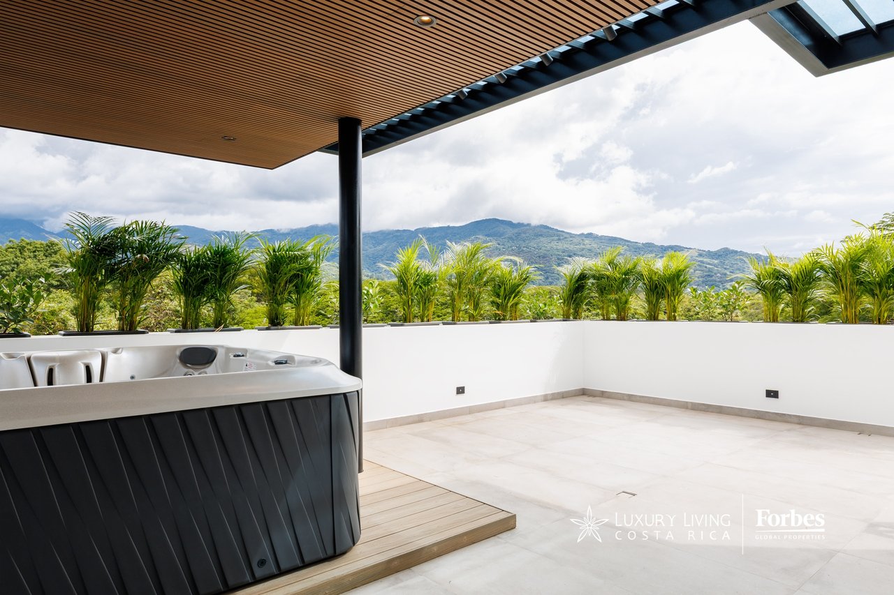 Rooftop jacuzzi beneath a wood canopy, with tropical palms and mountain views.