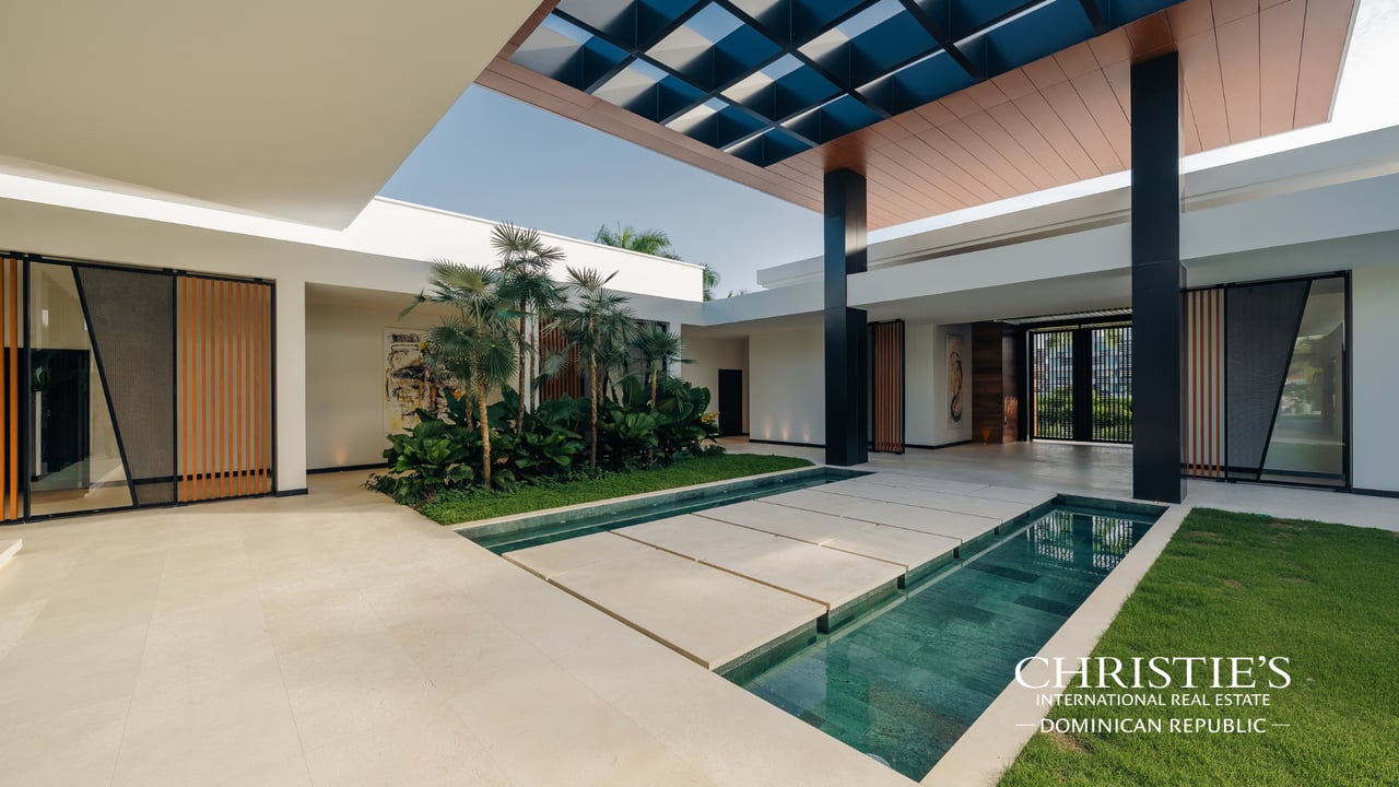 Modern villa courtyard with a narrow turquoise pool, broad stepping stones, and tropical landscaping.