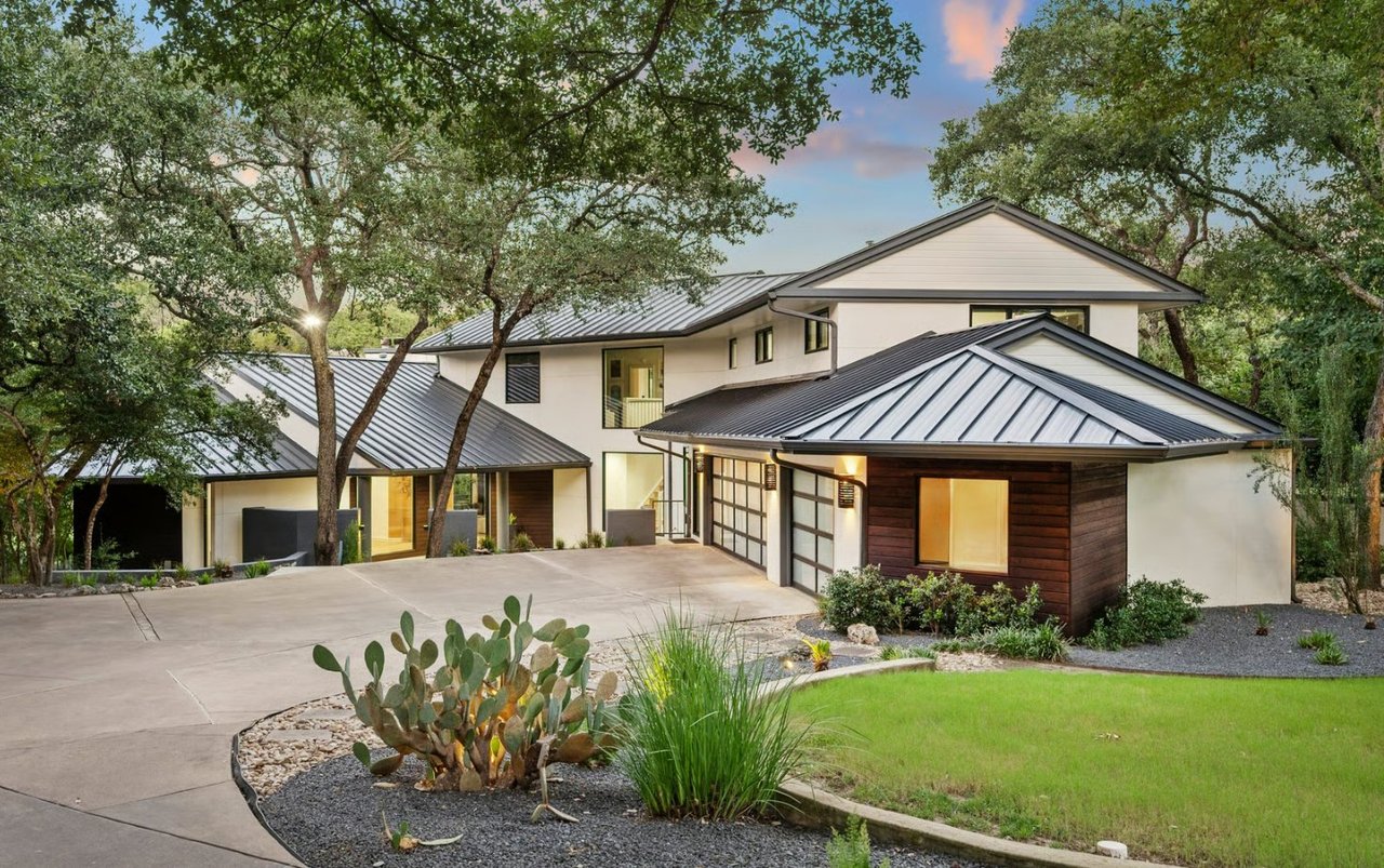 Modern home with metal roofs and dark wood accents framed by mature oak trees.