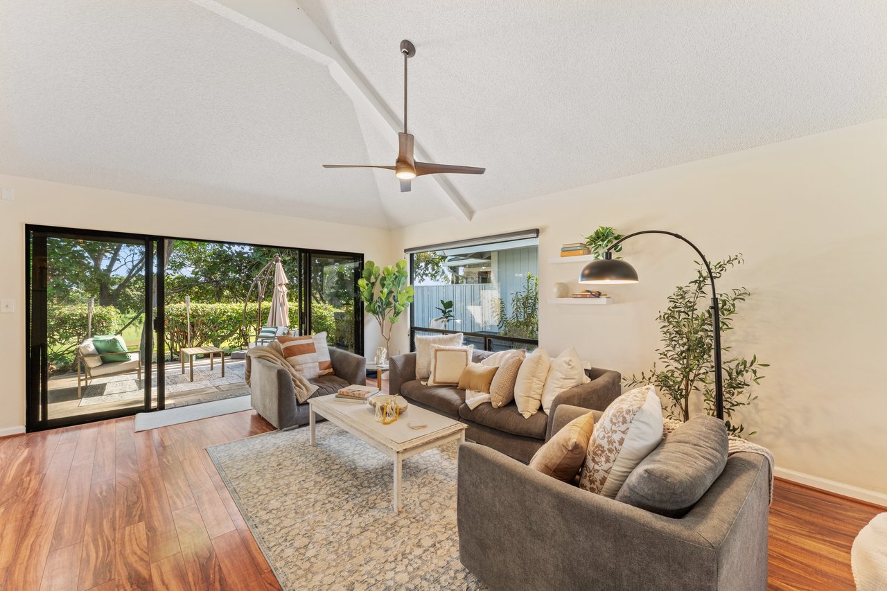 Living room with gray sofas, vaulted ceiling, and sliding glass doors opening to a leafy patio.