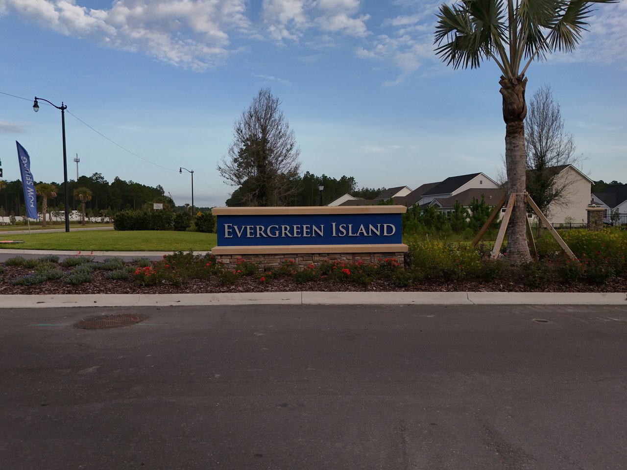 Evergreen Island entrance sign beside the road, with homes and palm trees in the background.
