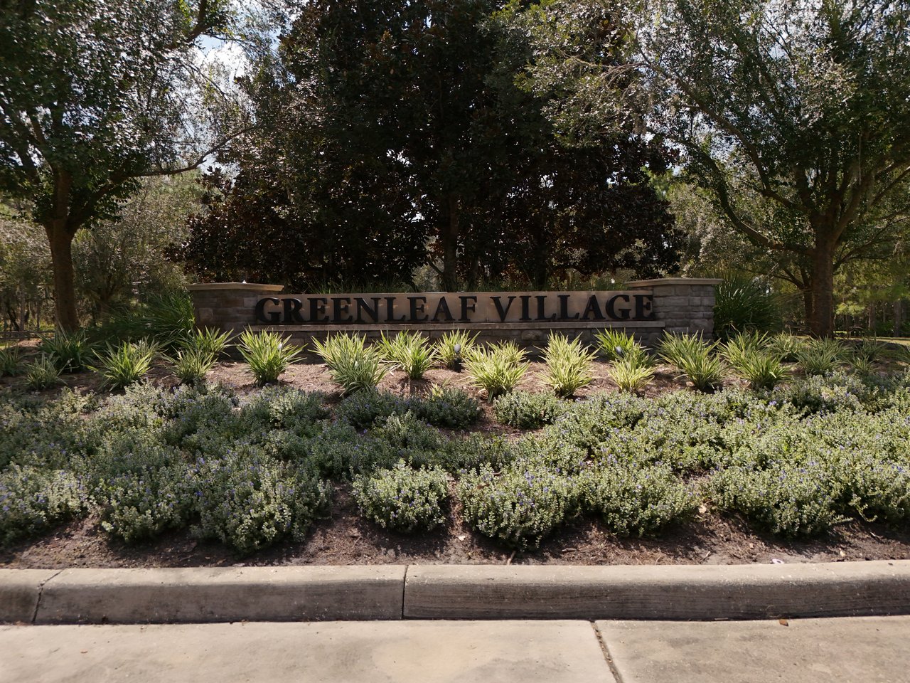 Greenleaf Village entrance sign set among landscaped beds and mature trees.