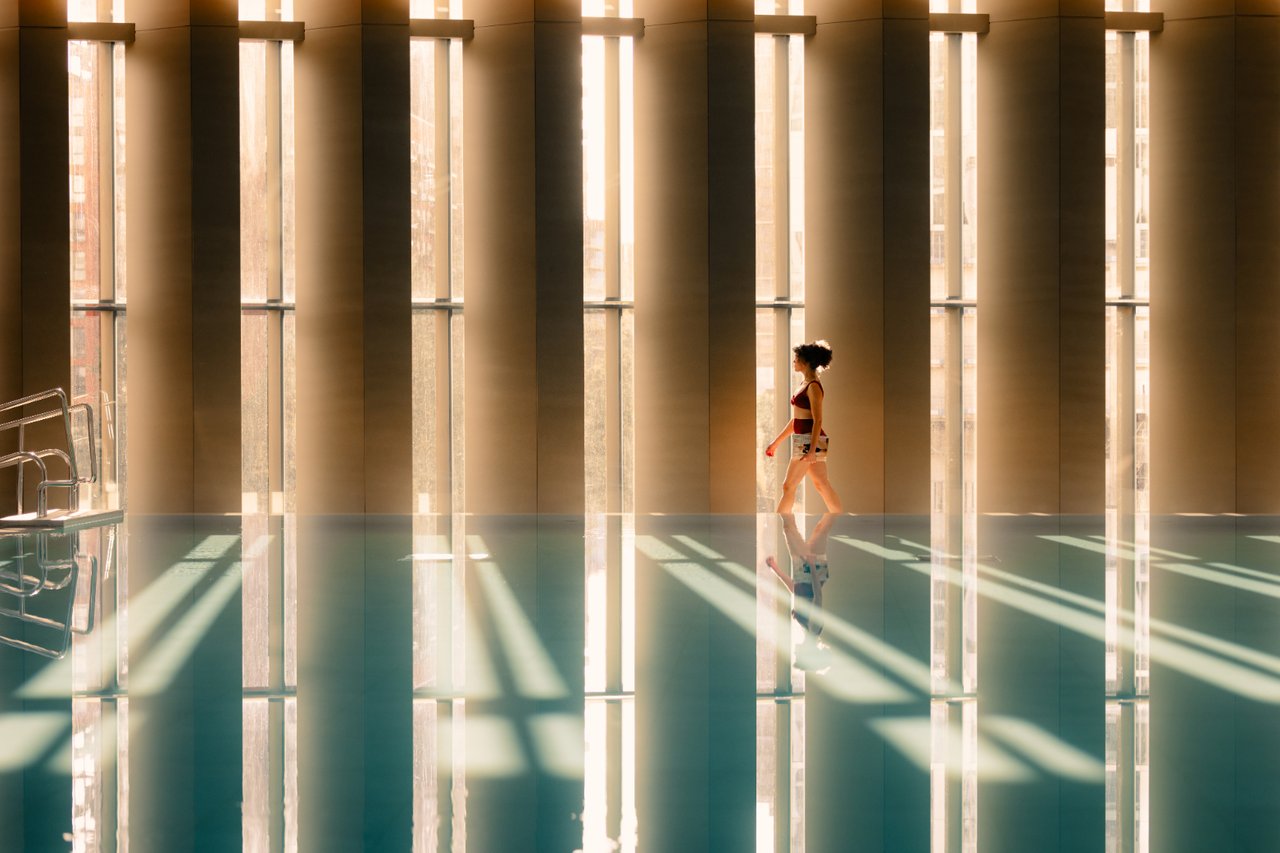 Indoor pool with tall windows and bronze columns, sunlight reflecting across the water.