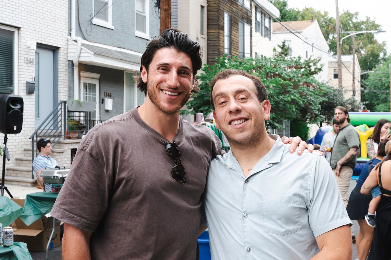 Two men smile together at a neighborhood block party on a residential street.