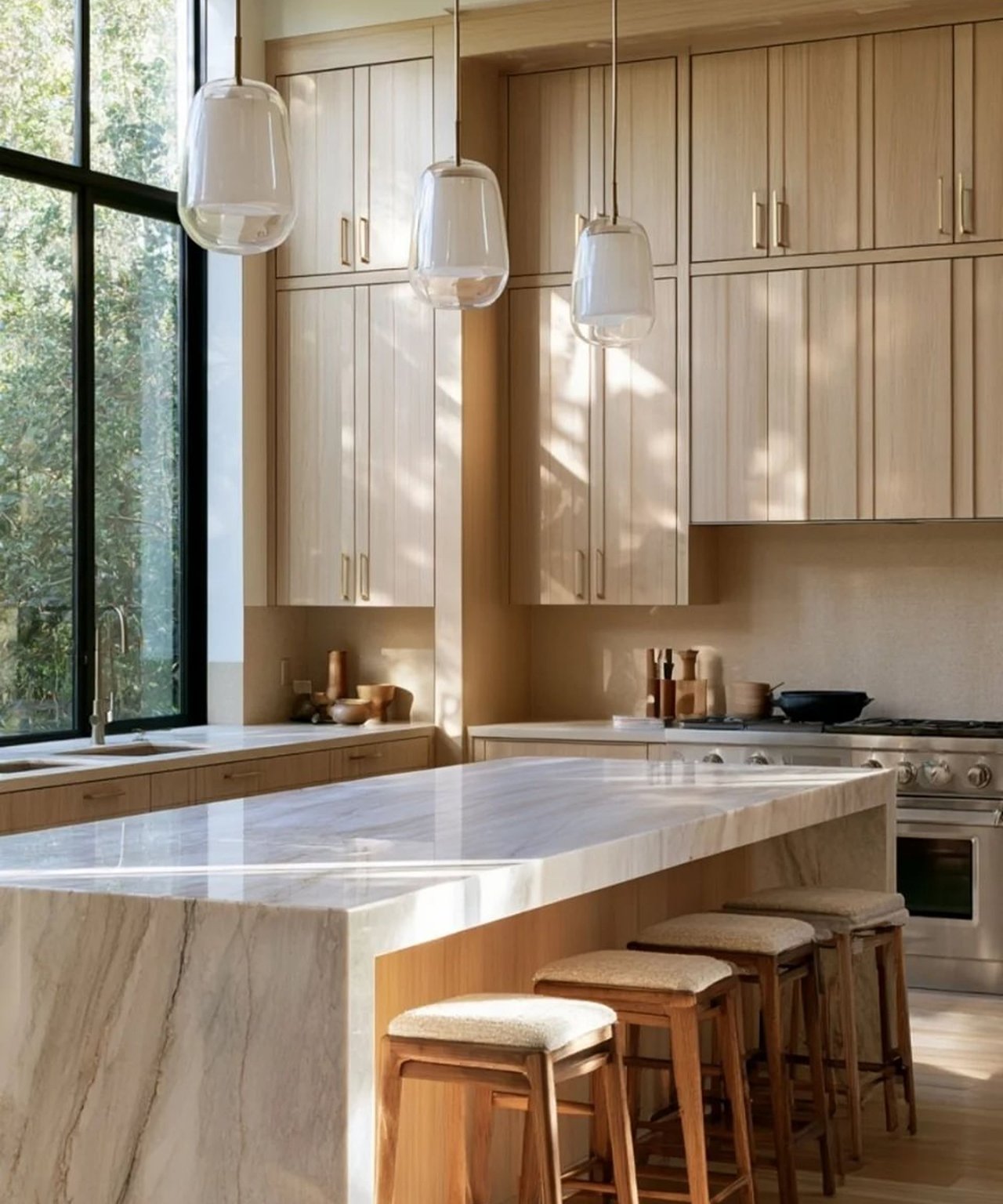 Modern kitchen with a veined marble island, light wood cabinets, and three glass pendant lights.