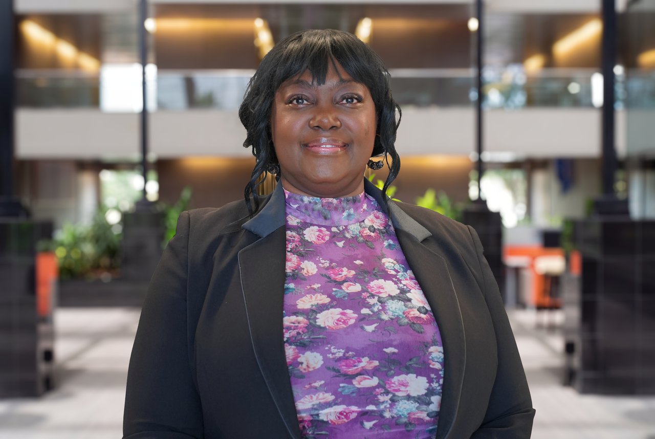 Sherry Thomas in a black blazer and purple floral blouse in a modern office lobby.